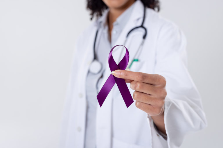 Midsection of african american mid adult female doctor holding purple cancer awareness ribbon. white background, epilepsy, pancreatic cancer, doctor, medical, awareness, support and healthcare